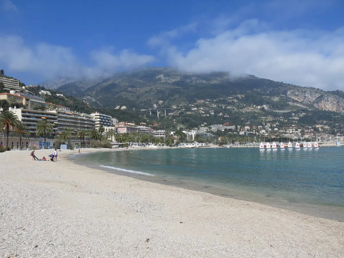 Plage des Sablettes à Menton, sable clair et mer turquoise devant les montagnes
