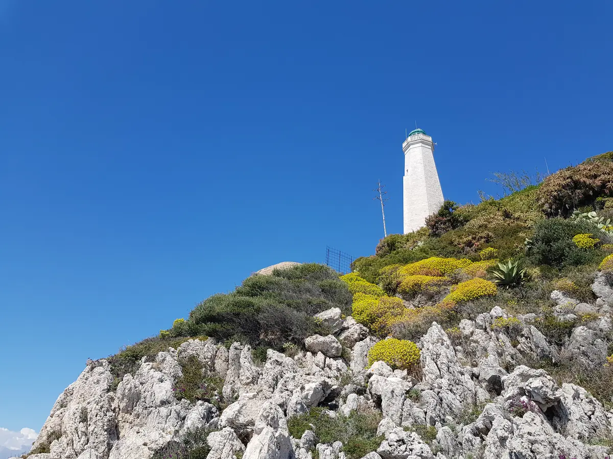 Le phare blanc du cap Ferrat au-dessus des rochers et de la garrigue